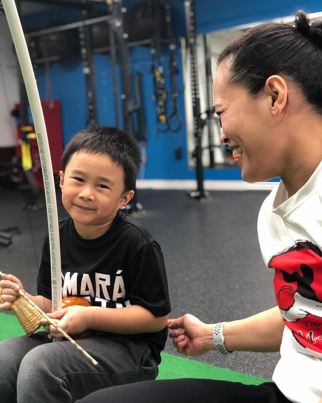 Monitora Sorriso teaching a child student how to play a berimbau